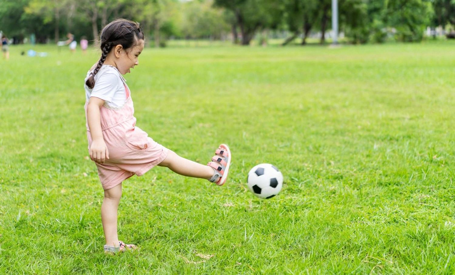 Young girl kicking a football on green grass during an outdoor school break
