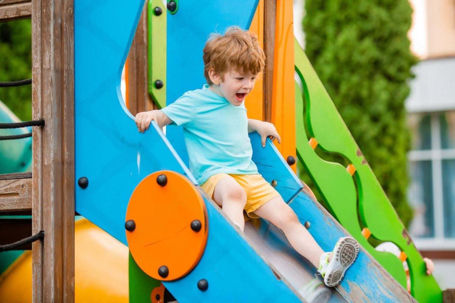 Happy young boy sliding down a colourful playground slide during break time