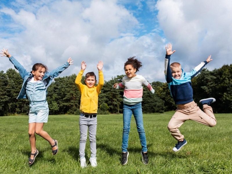 Group of younger students jumping and playing outside on a school field