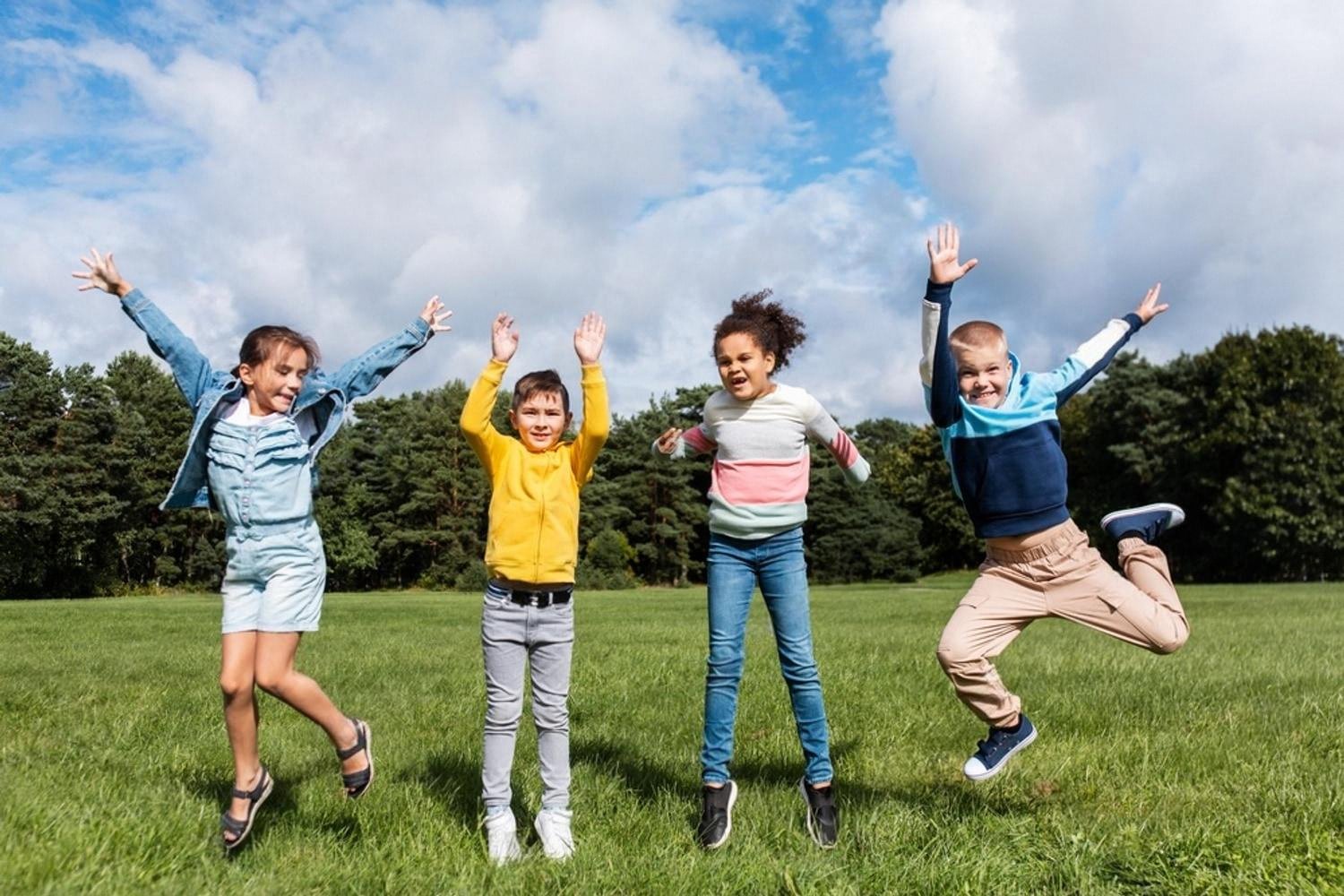 Group of younger students jumping and playing outside on a school field
